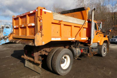 Orange International dump truck with hooklift bed seen from rear-left showing raised bed and dual rear wheels.
