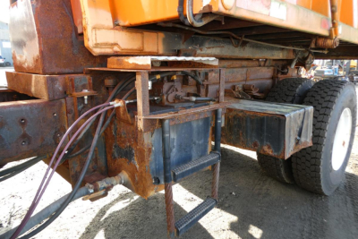Truck rear undercarriage with rusty metal frame and hydraulic lines near a hooklift system.