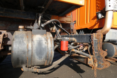 Air tank and hydraulic lines on side of hooklift truck showing cylindrical reservoir and red filter with hoses and rusted metal framework