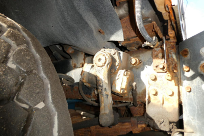 International truck front suspension/engine bay with rusted metal components and hooklift linkage visible.