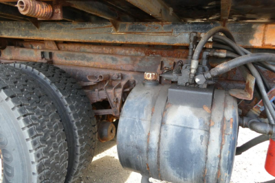 International truck undercarriage showing hydraulic reservoir and hoses with wheel and frame rust from side view