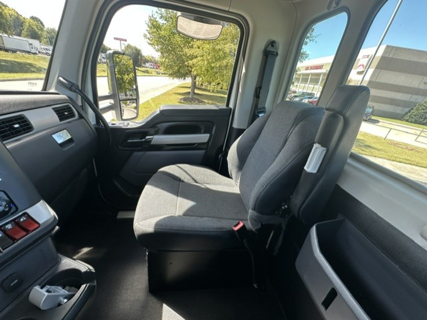 Kenworth T880 cab interior showing driver and passenger seats with gray fabric, dashboard, steering wheel, and side window view.