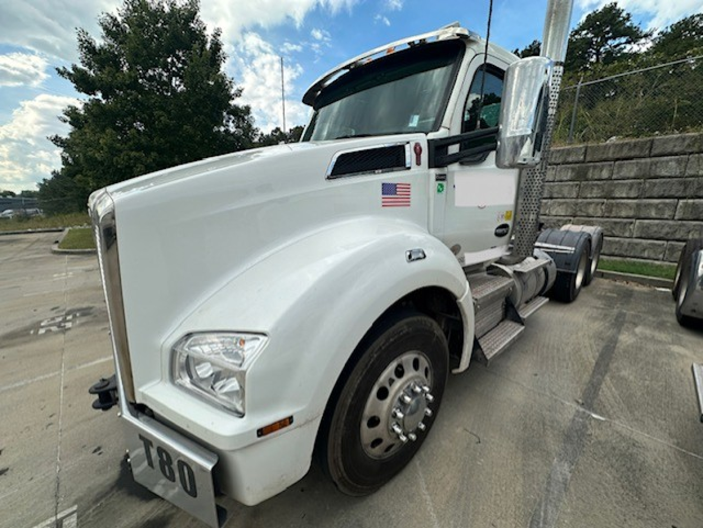Kenworth T880 conventional daycab tractor in white, front-left view showing cab, front fender, and dual rear wheels, with U.S. flag sticker on door and chrome steps.