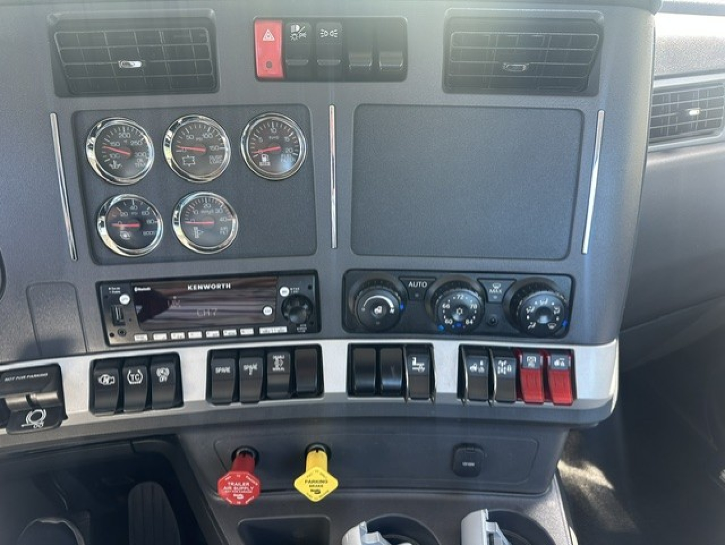 Kenworth T880 dash area with multiple gauges, switches, and controls; center stack shows Kenworth radio; climate knobs and two colored keys visible.