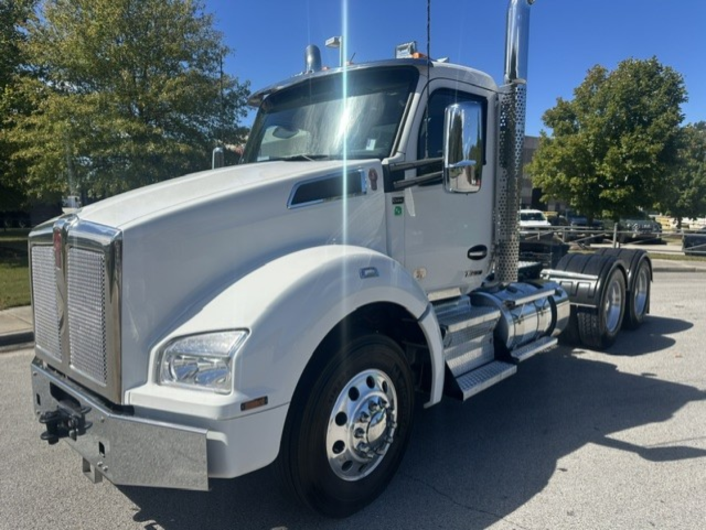 Kenworth T880 daycab truck in white, front-left view showing chrome grille, large mirrors, dual exhaust stacks, fuel tanks, and front bumper. No visible logos or text legible.