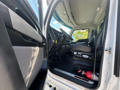 Kenworth T880 truck cab interior showing driver's seat, steering wheel, dashboard, and a red fire extinguisher mounted under the seat.