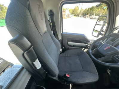Truck interior showing driver seat and steering wheel with view through windshield; Kenworth branding on seat and dashboard area visible.