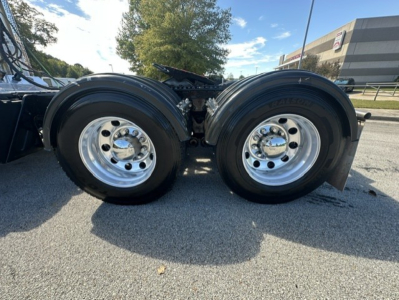 Kenworth T880 dual rear axle wheels and suspension near cab area, chrome rims with black tires, side view showing tandem axle configuration.