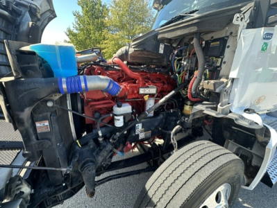 Kenworth T880 engine bay showing diesel engine with red components, blue hose, wiring harness, and front wheel well.