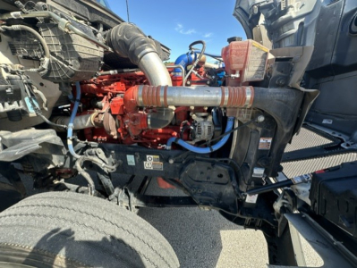 Kenworth T880 engine bay view showing red engine block, blue hoses, and silver exhaust components.