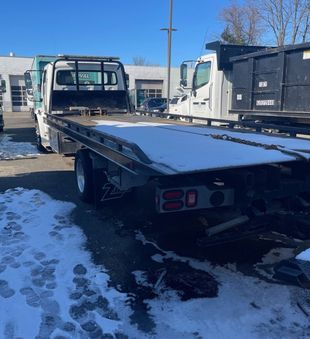 Flatbed tow truck with extended carrier on a Freightliner M2 106 chassis, rear view showing bed and taillights.