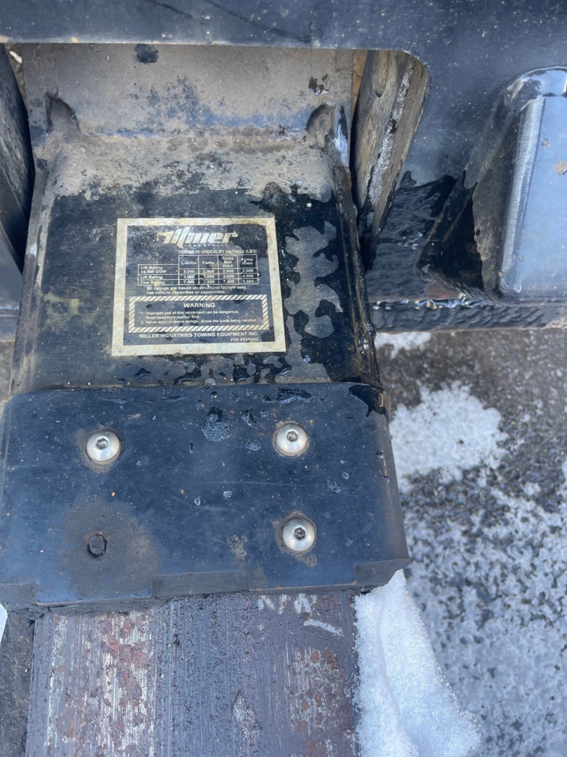 Close-up of a label on a Freightliner M2 106 chassis showing model plate with technical specs, bolts, and surrounding metal surface with snow and grime.