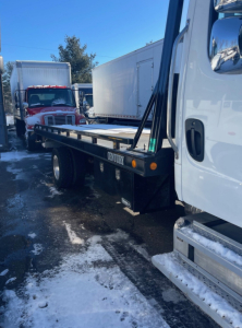 Truck bed on a Freightliner M2 106 with tow truck body, side view shows flatbed and part of cab, some snow on ground.