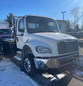 White 2019 Freightliner M2 106 Medium D tow truck front-left view showing chrome bumper, grille, dual step access, and cab; signage and snow on ground.