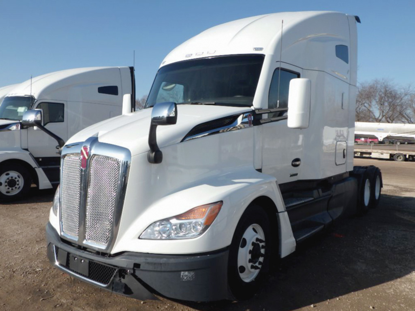 Truck front view of a white 2023 Kenworth T-680 Next Gen with sleeper cab, large chrome grille, dual side mirrors, and daytime running lights.