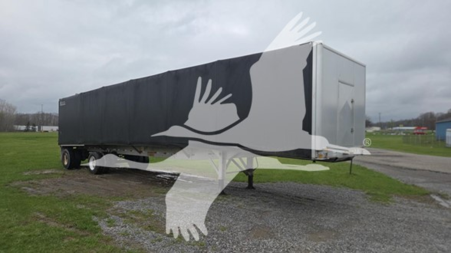 Curtainside trailer with black covered cargo area; front neck and kingpin visible; long rectangular trailer with rear door panel. Overlayed watermark of birds in flight across image.