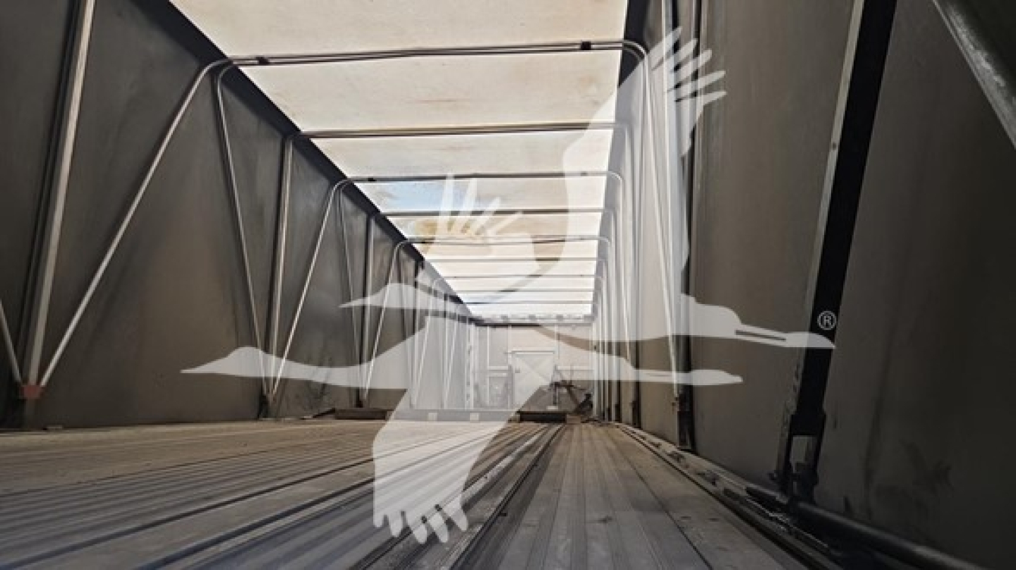 Curtainside trailer interior with ribbed metal floor and side rails, opening toward the rear, perspective shot.