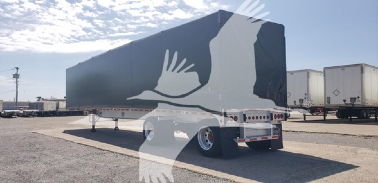 Flatbed trailer showing its side with tandem axles and rear loading doors.