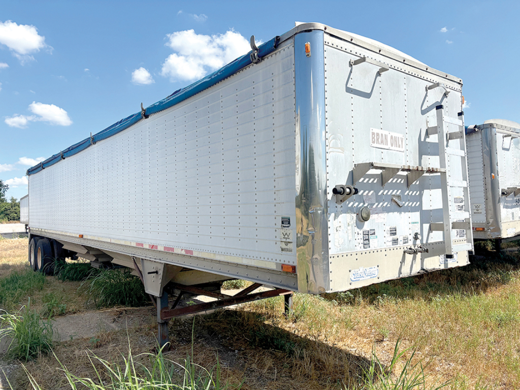 Trailer side view showing a 2003 Wilson Pacesetter hopper trailer with metal paneling, blue rails, and rear access with toolbox and Br*** panel. VIN 1W1MCF1W73A236650 visible.