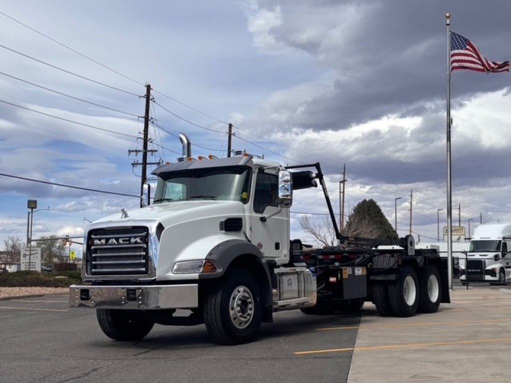 2027 Mack GR64B roll-off truck in a parking lot, side view showing large chrome grille, dual rear axles, and exposed exhaust stacks.