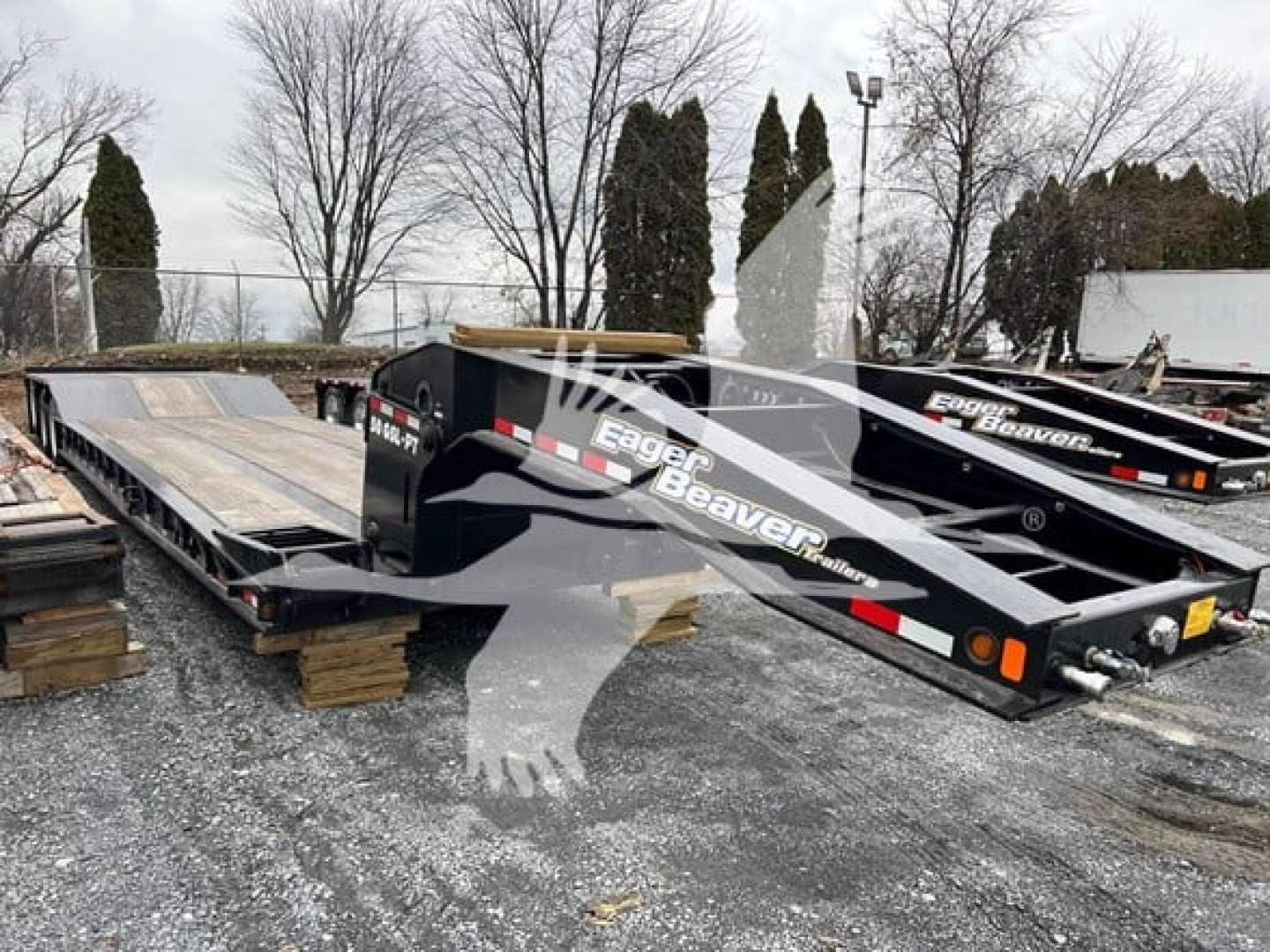 Truck trailer in a yard showing lowboy flatbed with Eager Beaver branding and ramp sections, black with white graphics.