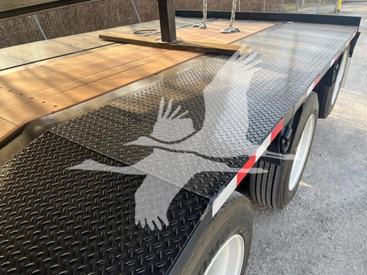 Trailer deck with diamond plate steel and wooden sections; two axles with white rims and black tires, part of a lowboy trailer.