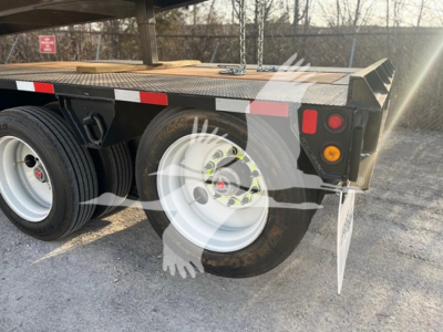 Trailer rear view showing dual rear wheels on a flatbed lowboy trailer with white rims, black fenders, and reflective red/white tape along the edge.