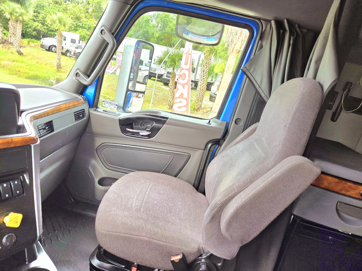 Interior of a 2021 International LT625 truck cab showing driver seat and dashboard with grey fabric seats and wood trim.