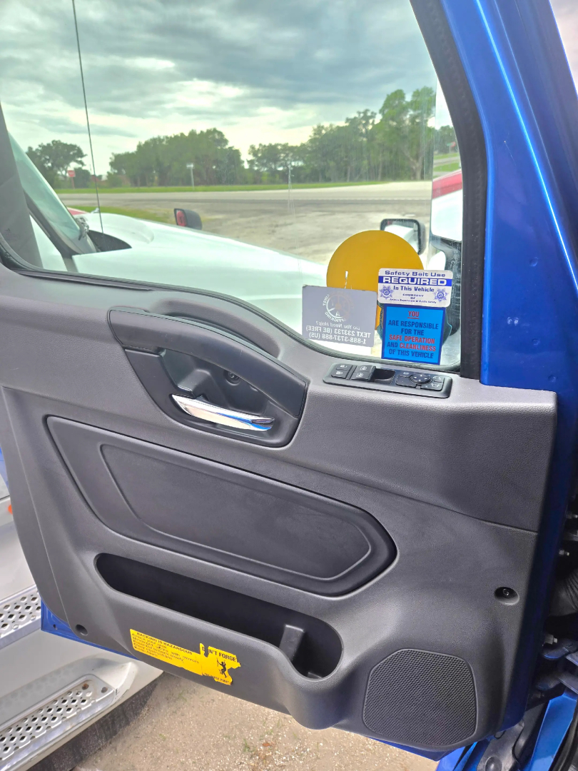 Truck interior door panel showing window controls and stickers on the dashboard area; blue exterior visible through open door