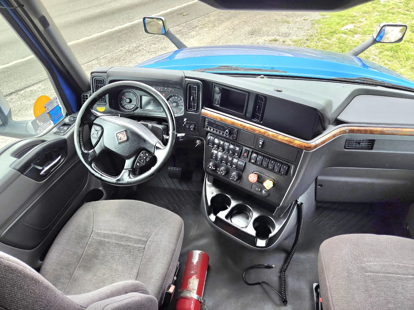 Interior of 2021 International LT625 truck cab showing steering wheel, dashboard with radios, controls, cup holders, and front seats.
