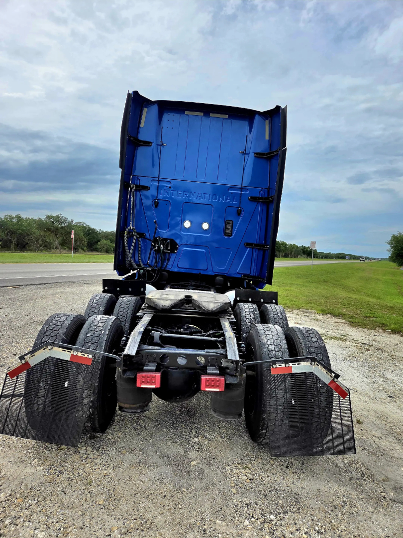 Tractor-trailer rear view showing chassis and dual rear axles with mud flaps and blue cab shell raised.