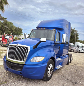 Blue 2021 International LT625 tractor-trailer cab, front three-quarter view, with chrome grille, side mirrors, and sleeper cab; appears in a lot with other trucks.