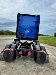 Tractor-trailer rear view showing chassis and dual rear axles with mud flaps and blue cab shell raised.