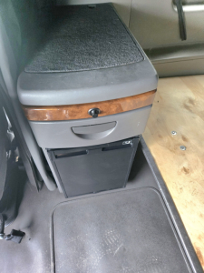 Cab interior showing a storage drawer below a brown wood trim and a small black refrigerator in a 2021 International LT625 sleeper truck.