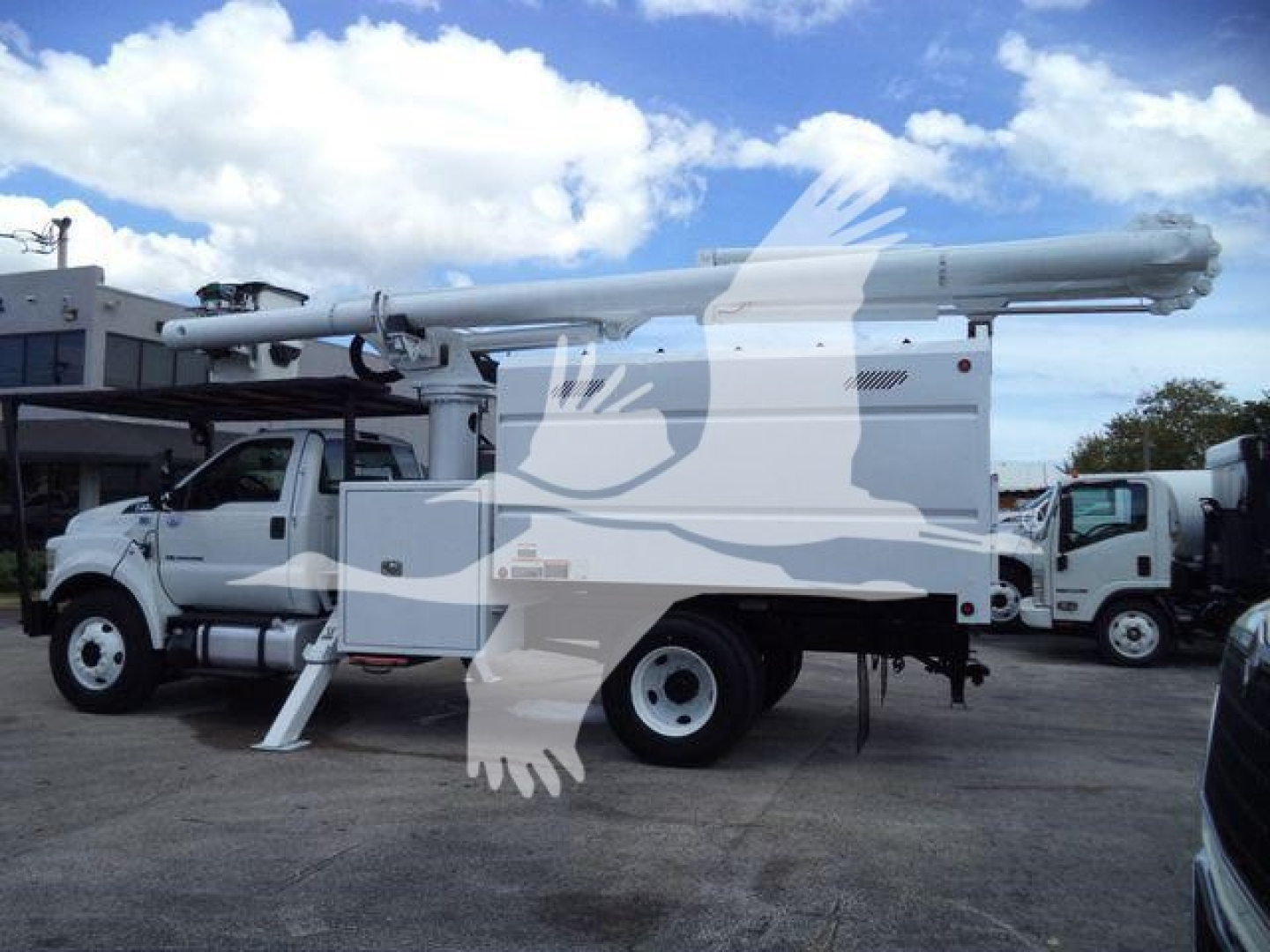 Ford F750 bucket truck with elevated boom in service bay. Side view shows white utility body, stabilizers, and boom resting on top.