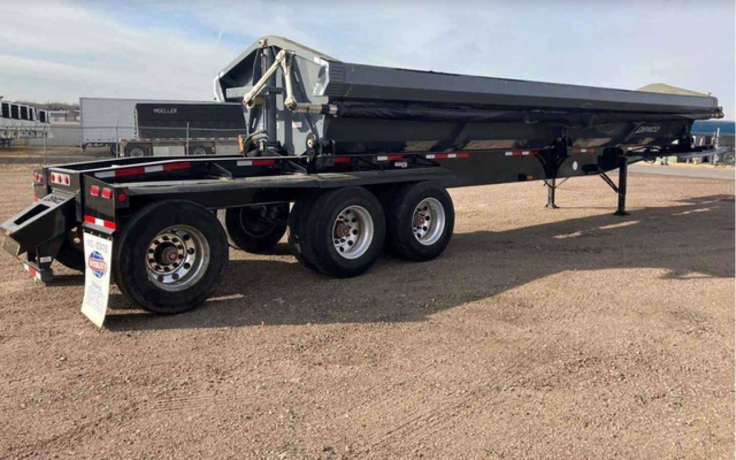 Demco side dump trailer shown in side view with tandem axles and folded bed in raised position.