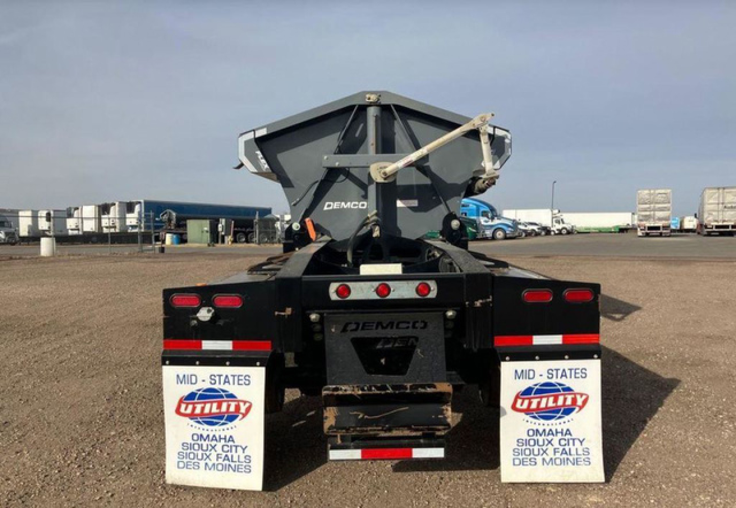 Demco side dump trailer rear view showing mud flaps and hydraulic bed mechanism with Demco branding.