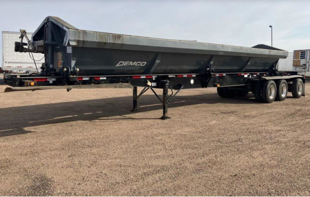 Demco side dump trailer in side view showing undercarriage and tandem axles with Demco branding on the hopper.