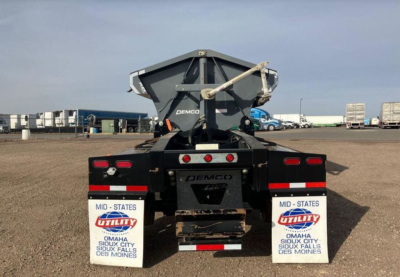 Demco side dump trailer rear view showing mud flaps and hydraulic bed mechanism with Demco branding.