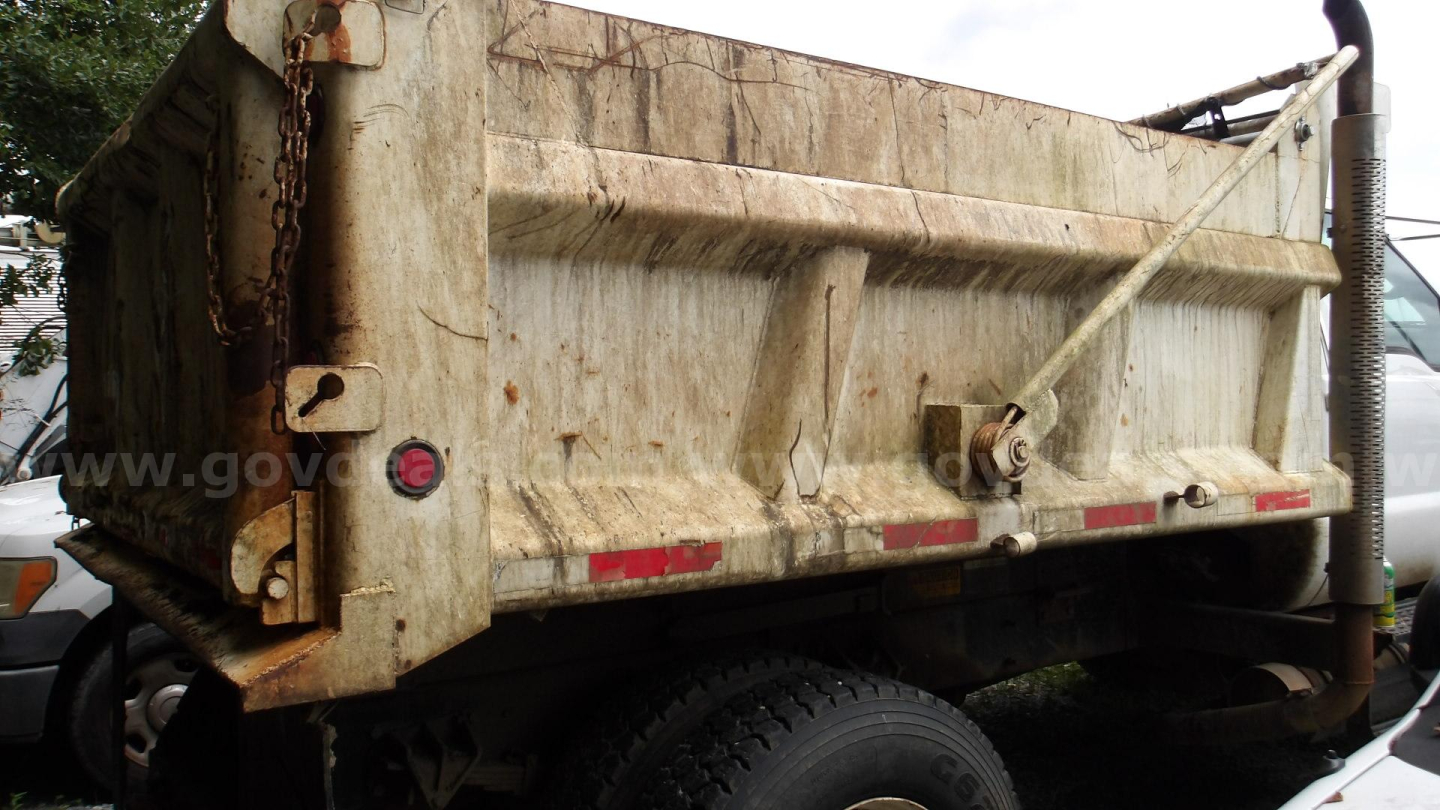 Dump truck bed of a 2009 Ford F-750 in-service view showing dirty cargo bed with chain lift and rear tailgate hardware.