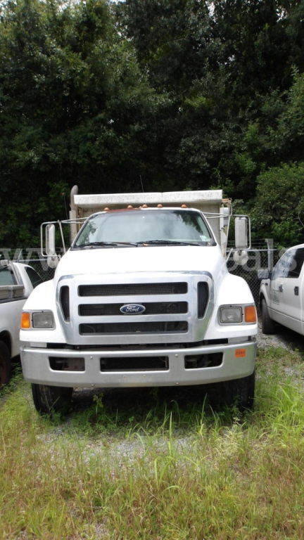 White Ford F-750 dump truck front view showing grille, headlights, and large side mirrors in a grassy lot.