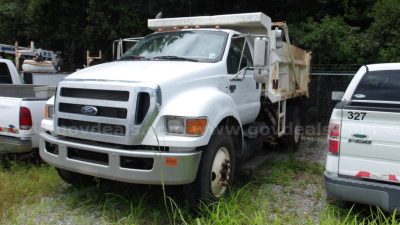 Ford F-750 dump truck in a lot showing front three-quarter view with white cab and dump bed, surrounding vehicles.