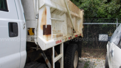 Truck bed of a 2009 Ford F-750 dump truck with white cab and rust accents on the dump bed showing side view and tire.