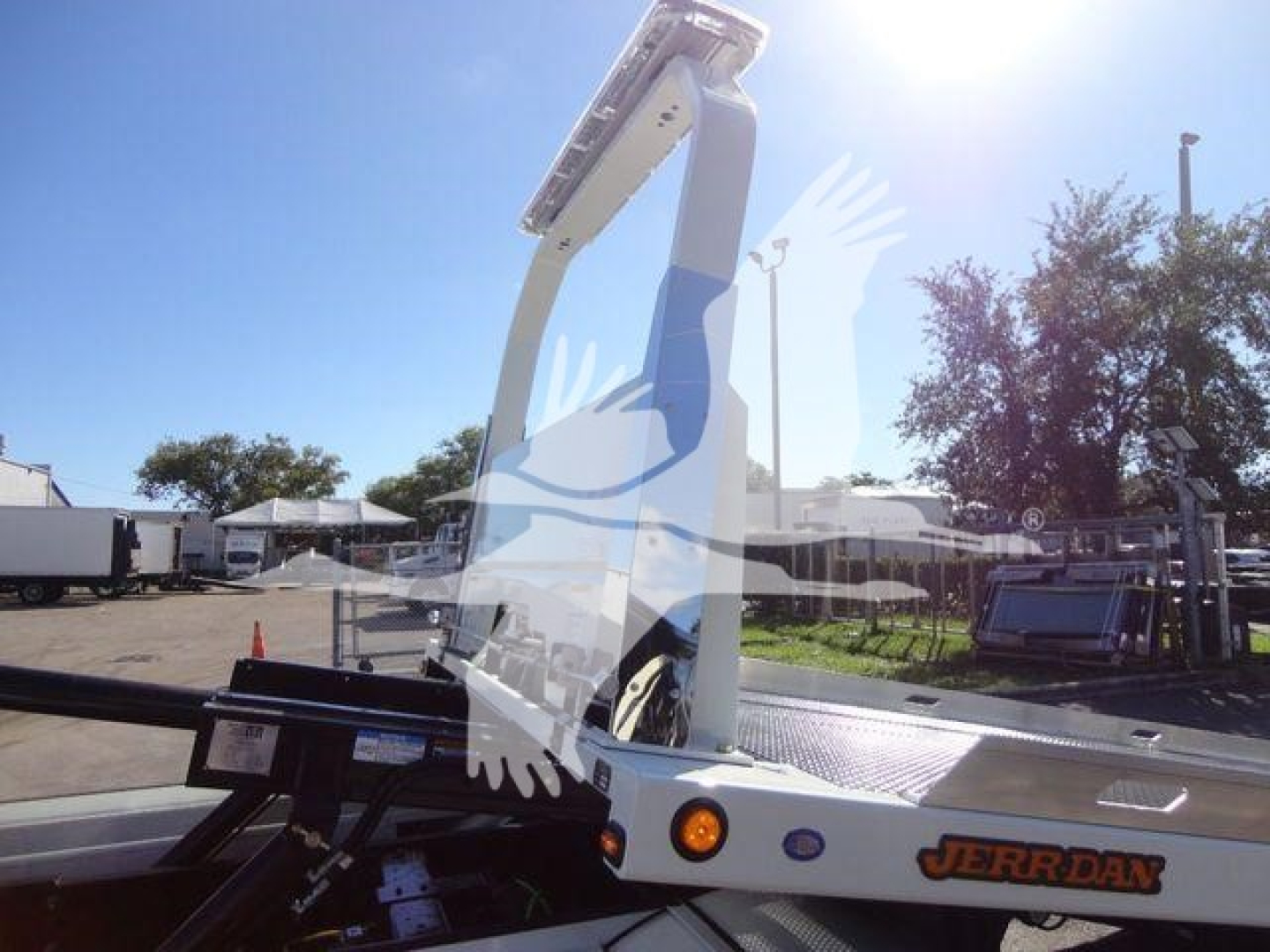 Truck equipment showing a white and black Jerr-Dan rollback carrier with a raised hydraulic arm in the bed and orange indicator lights. There is faint dealership watermark across the image.