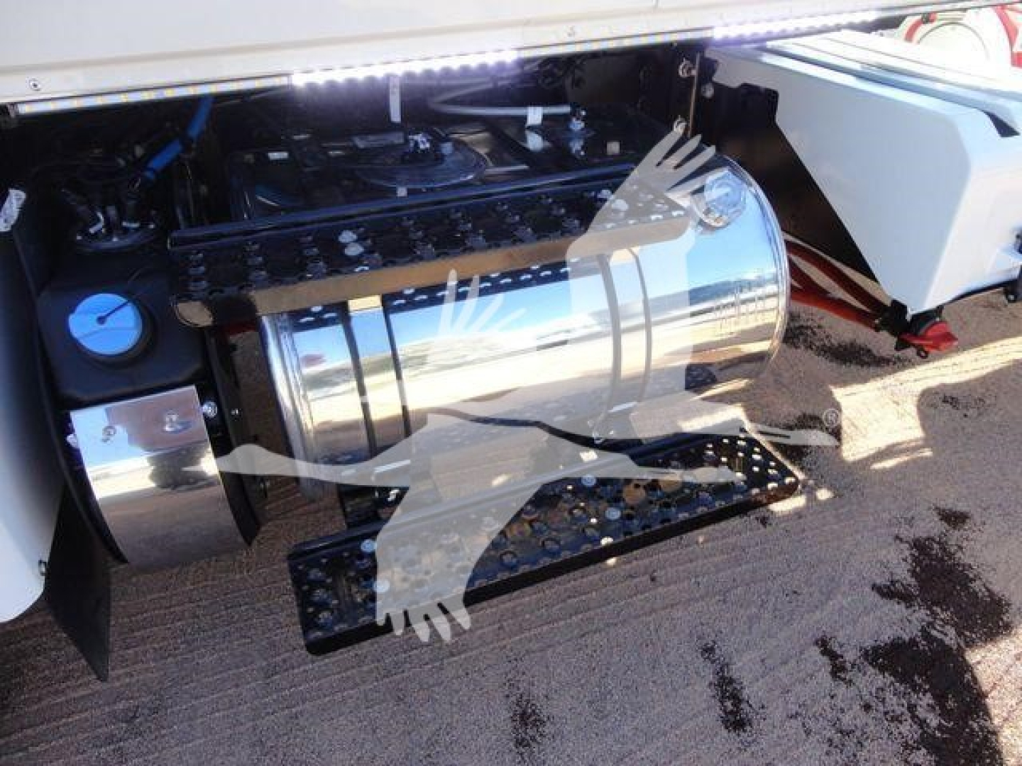 Truck engine bay with polished cylindrical fuel tank and chrome steps; view shows part of the engine compartment and mounting brackets.