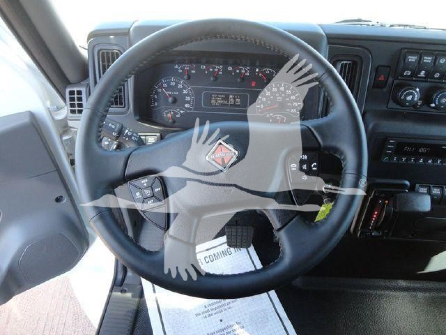 Truck cab interior with steering wheel and dashboard of an International MV, showing gauges and controls, stock badge overlayed.