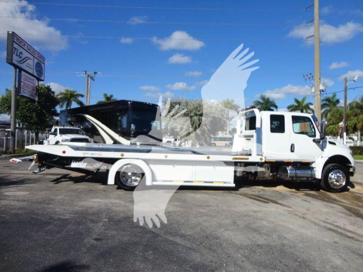 International MV tow truck with flatbed in side view showing stickered equipment and carrier truck bed.