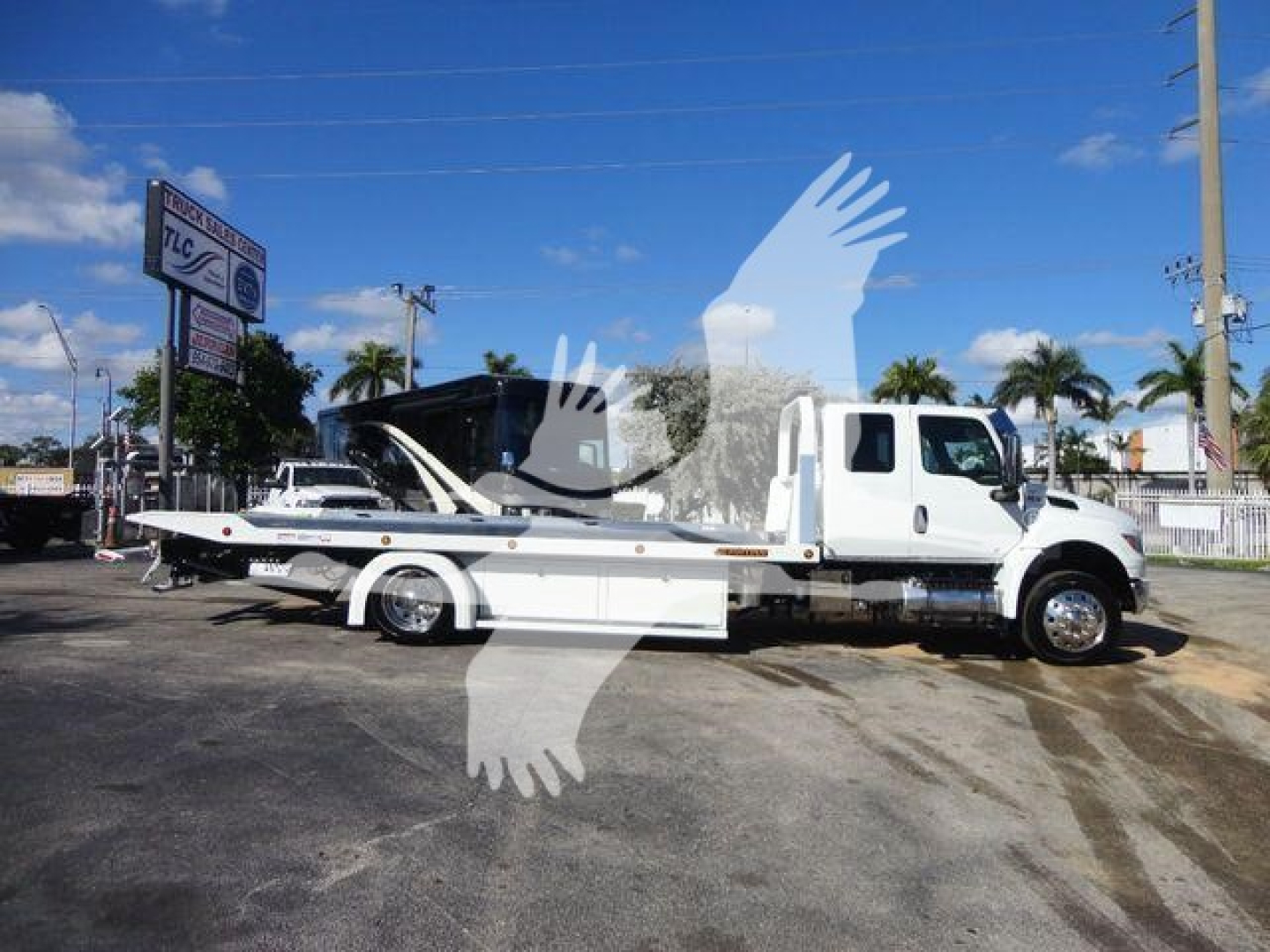Tow truck with a flatbed in service bay showing a white International MV chassis and long wheelbase flatbed.