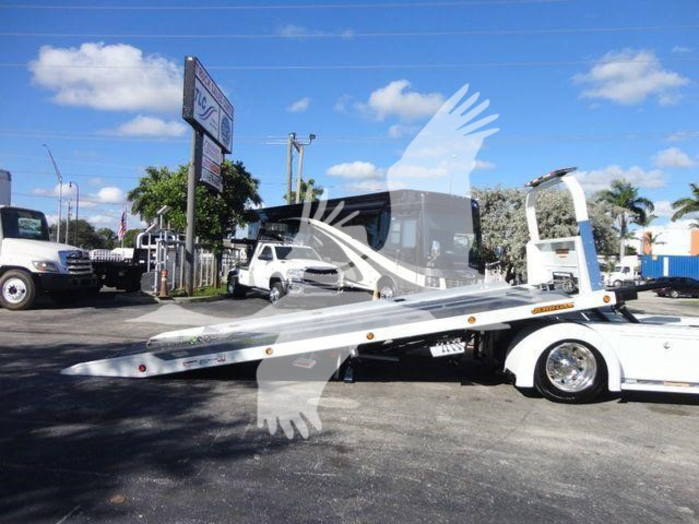 Tow truck flatbed with a raised white cab and a long metal loading bed extending from the rear, International MV model; clear blue sky