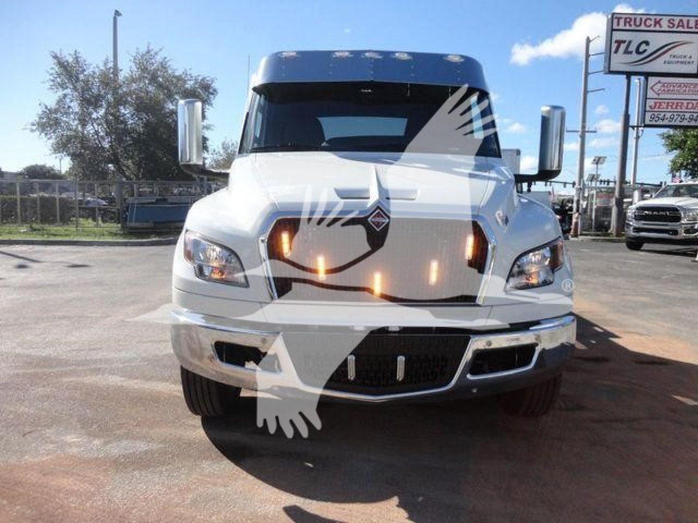 Truck front view showing International MV cab with emblem, large chrome grille, dual headlights, and daytime running lights; hood ornament and side mirrors visible.